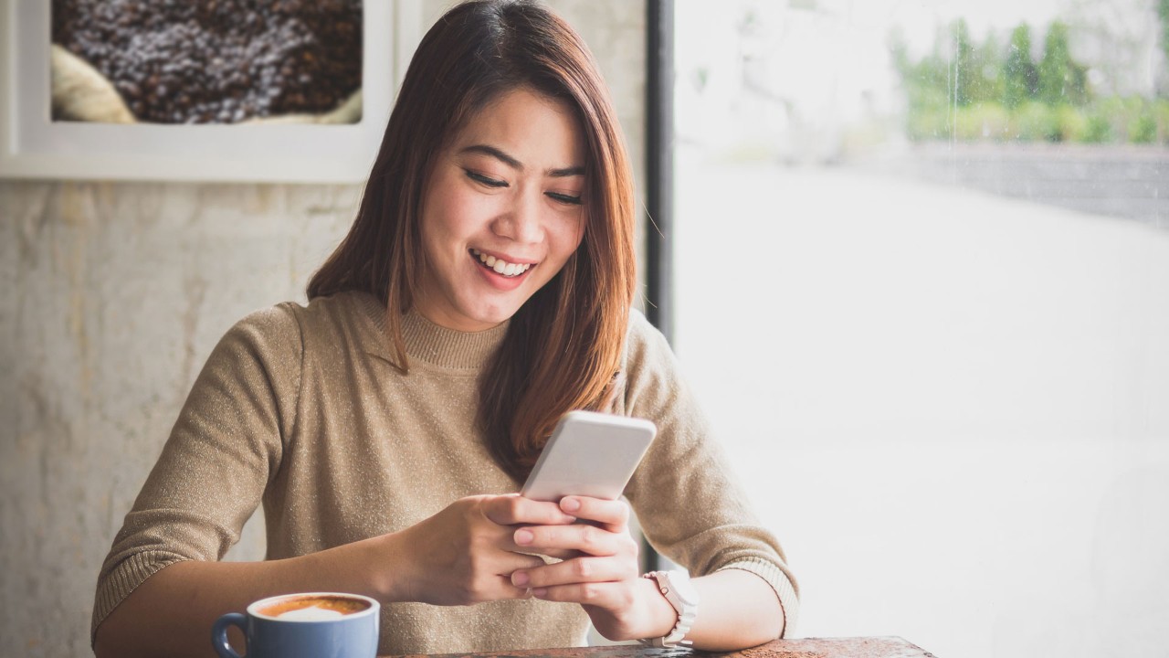 Girl holding mobile phone in coffee shop; image used for live within your means